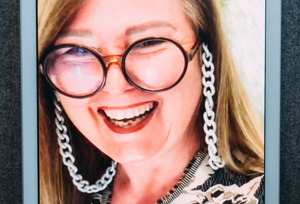 Frau mit langen Haaren und Brille sowie weißer Brillenkette blickt lächelnd von einem iPad zum Fotographen