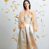 Model mit geöffnetem Federbolero, Faltenrock und Korsage in den Farben champagner und peach