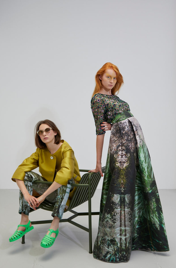 zwei junge Frauen die eine rothaarig die andere braunhaarig sitzen und lehnen an einem grünen Metallgartensessel und tragen ein Couture Top mit bodenlangem Designerrock mit Pflanzenmotiv sowie einen Lindgrünen Seidenmantel mit Hose aus der Art Edition