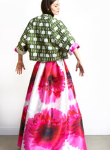 dunkelhaariges Model steht mit dem Rücken und trägt eine olivfarbene Kurzjacke mit pinken Rock mit großen Blumen