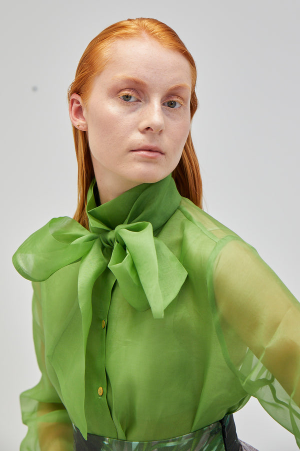 rothaarige junge Frau mit streng zurück gekämmten Haaren in apfelgrüner Seiden Organza Bluse mit großer Schleife