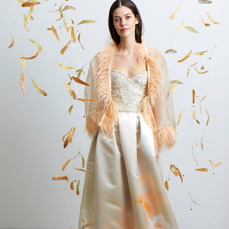 Model mit geöffnetem Federbolero, Faltenrock und Korsage in den Farben champagner und peach